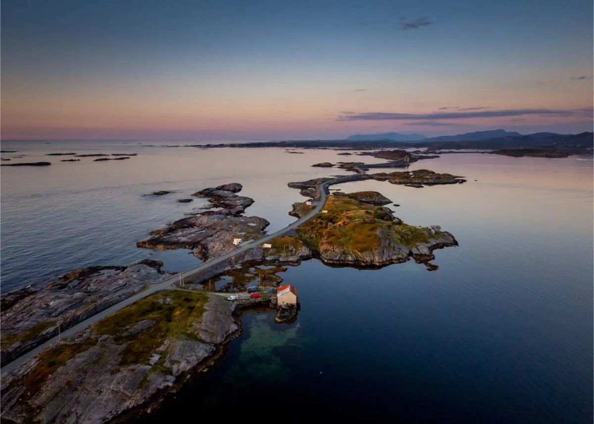 Aerial view of a road linking low rocky islets across calm sea, with a pink and blue sky at twilight