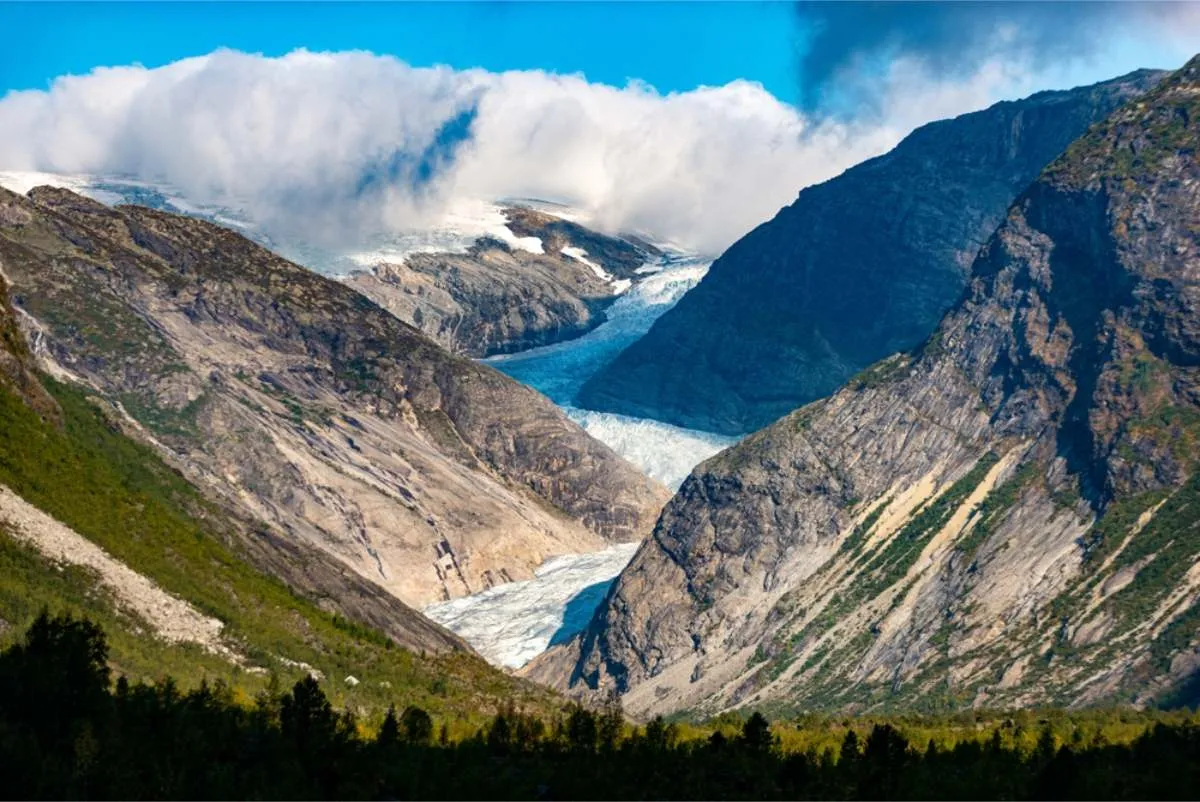 Blue glacier tongue flowing down between steep grey mountainsides