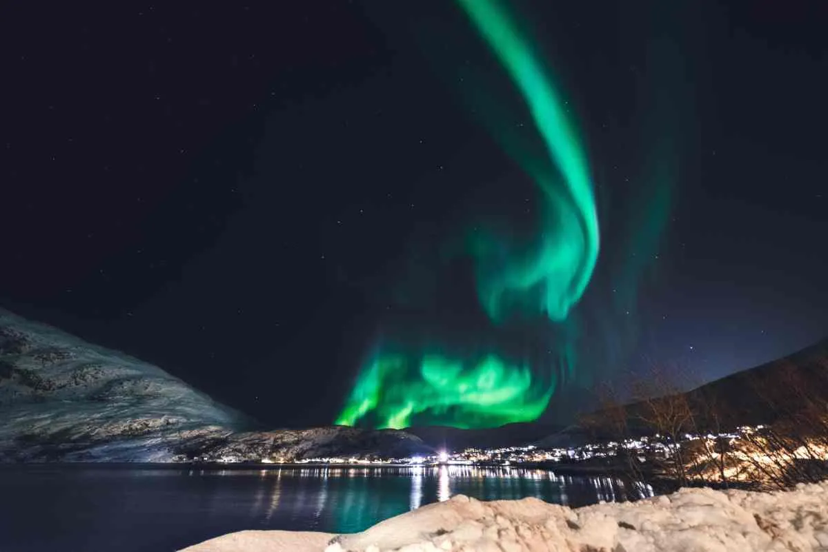 Northern lights glowing above Tromsø fjord on a clear winter night.