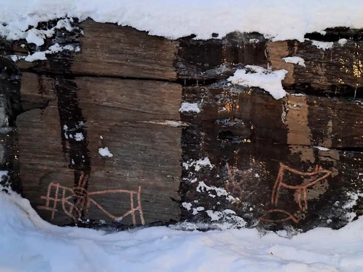 Ancient petroglyphs carved into rock, partially covered by snow.