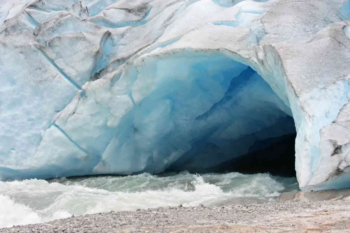 Blue ice cave at Jostedalsbreen glacier with meltwater rushing out across a rocky shoreline