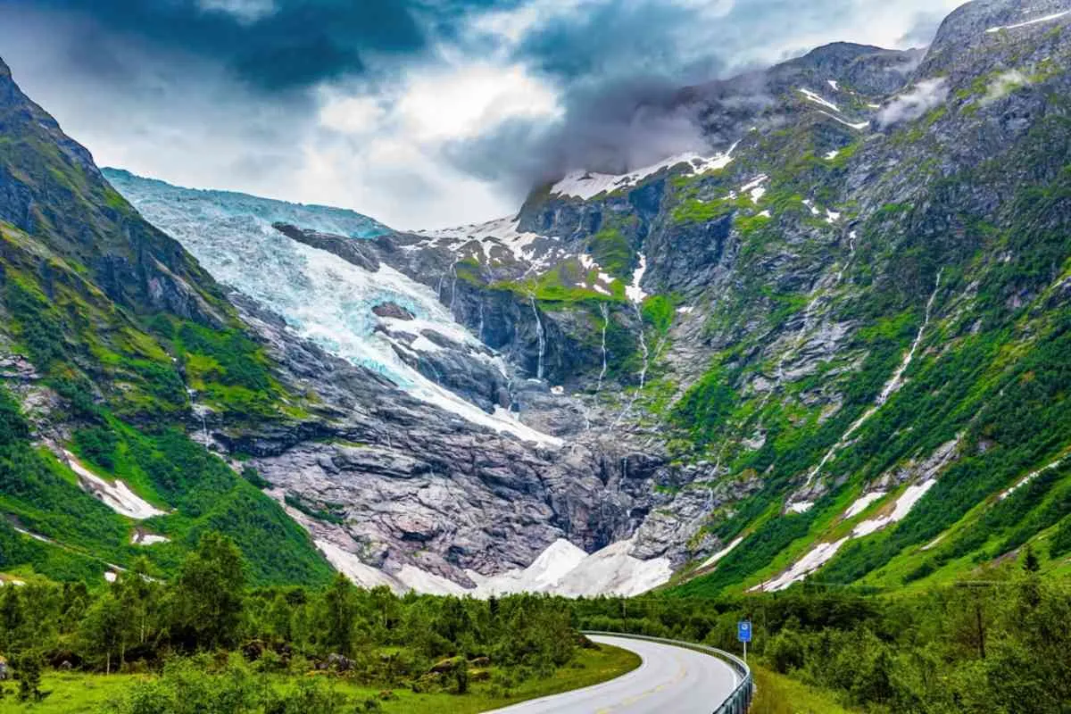 Mountain road leading toward Nigardsbreen glacier with dramatic clouds and green valley scenery