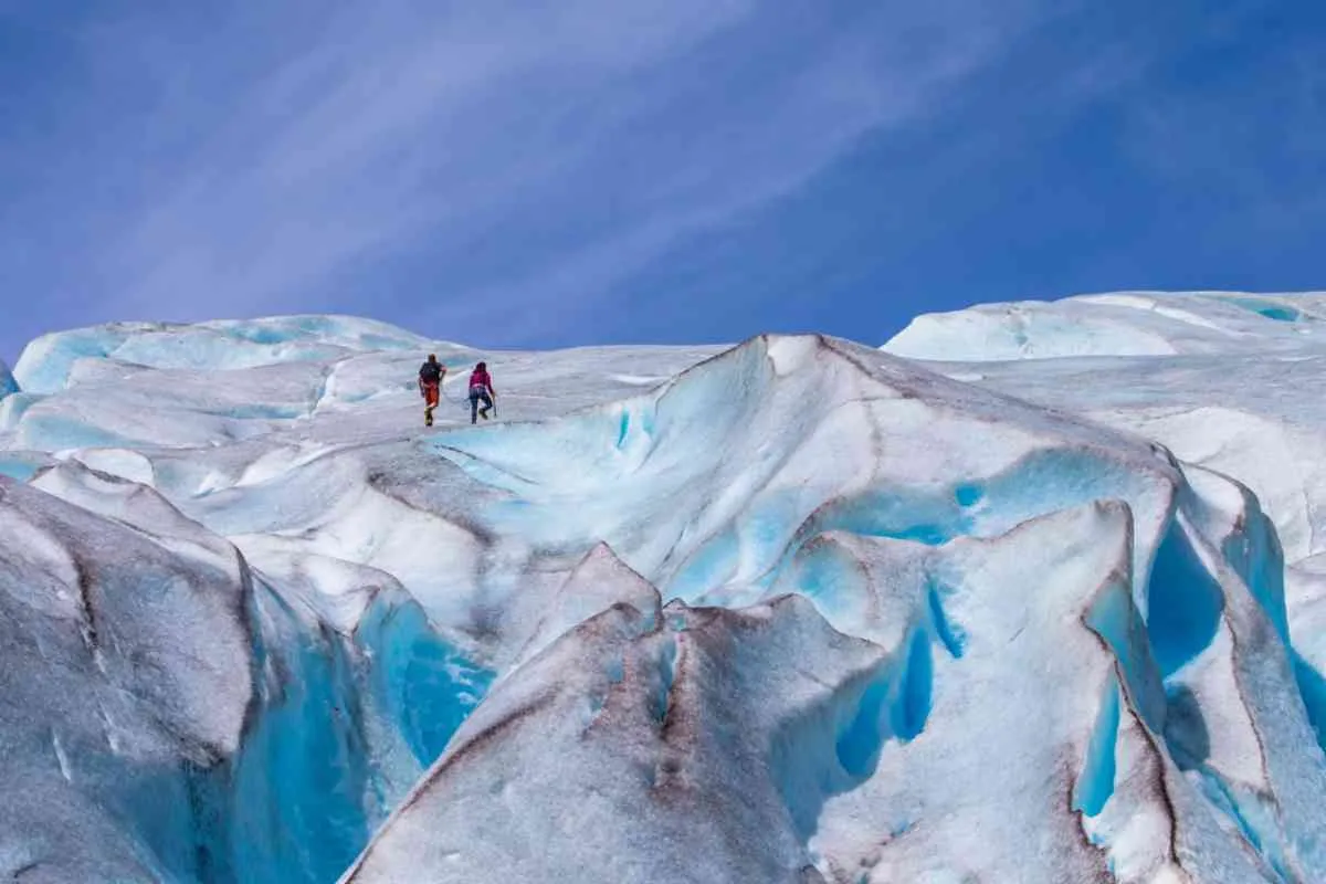 Two hikers walking across bright blue and white ice formations on Jostedalsbreen glacier
