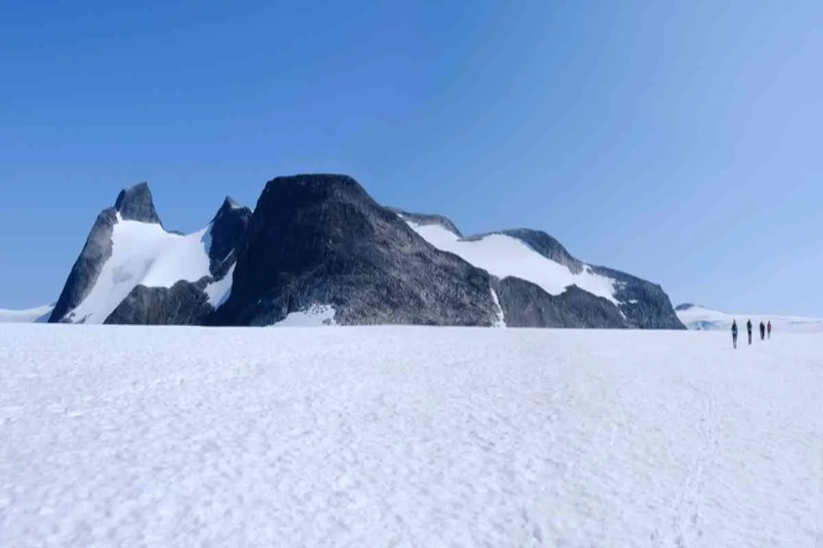 Tiny hikers crossing a vast snowfield below dark mountain peaks on Jostedalsbreen glacier