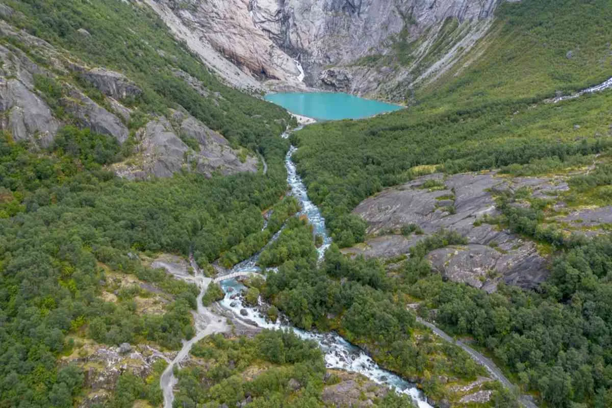 Aerial view of hiking trail and river leading to a turquoise glacial lake below Jostedalsbreen