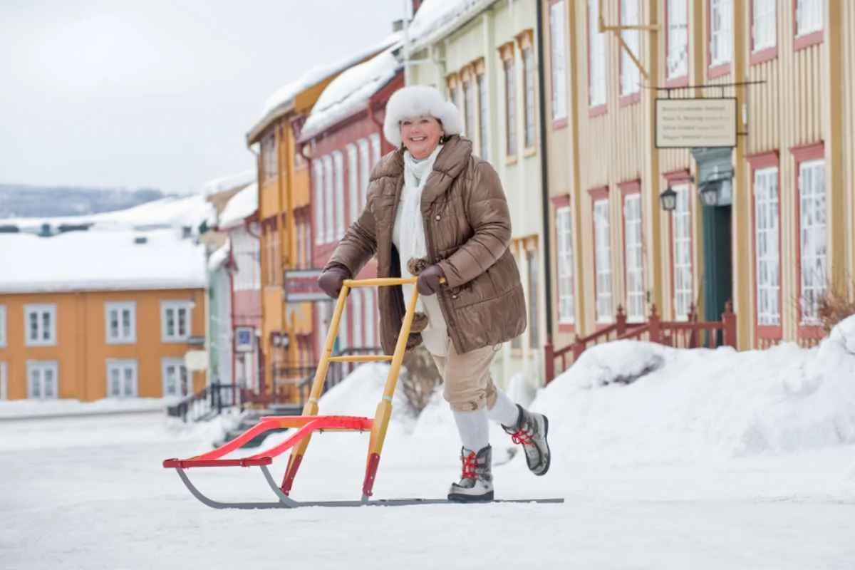Person using a kick sled on a snowy street in Røros, with colorful wooden houses lining the road in winter.