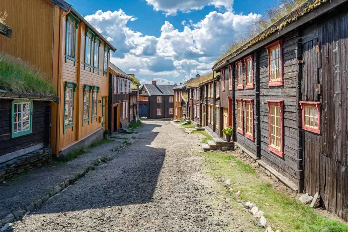 Charming lane in Røros with traditional wooden houses and grass roofs, leading toward the town center on a sunny day.