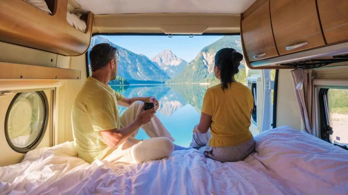 A couple enjoys beautiful views of a Norwegian lake from inside their camper while the vehicle remains parked.