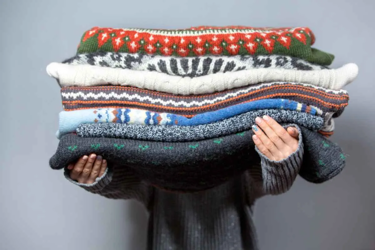 A person holds a huge amount of winter blankets and sweaters.
