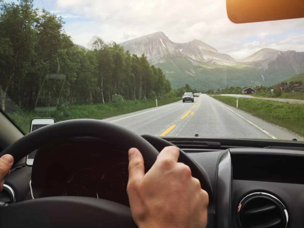 Hands hold the steering wheel of a vehicle as it travels along a Norwegian road.