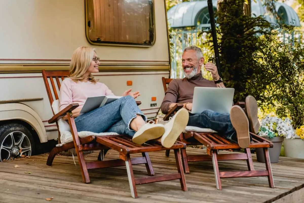 An elderly couple smilingly enjoys a well-deserved rest in sun loungers outside their camper