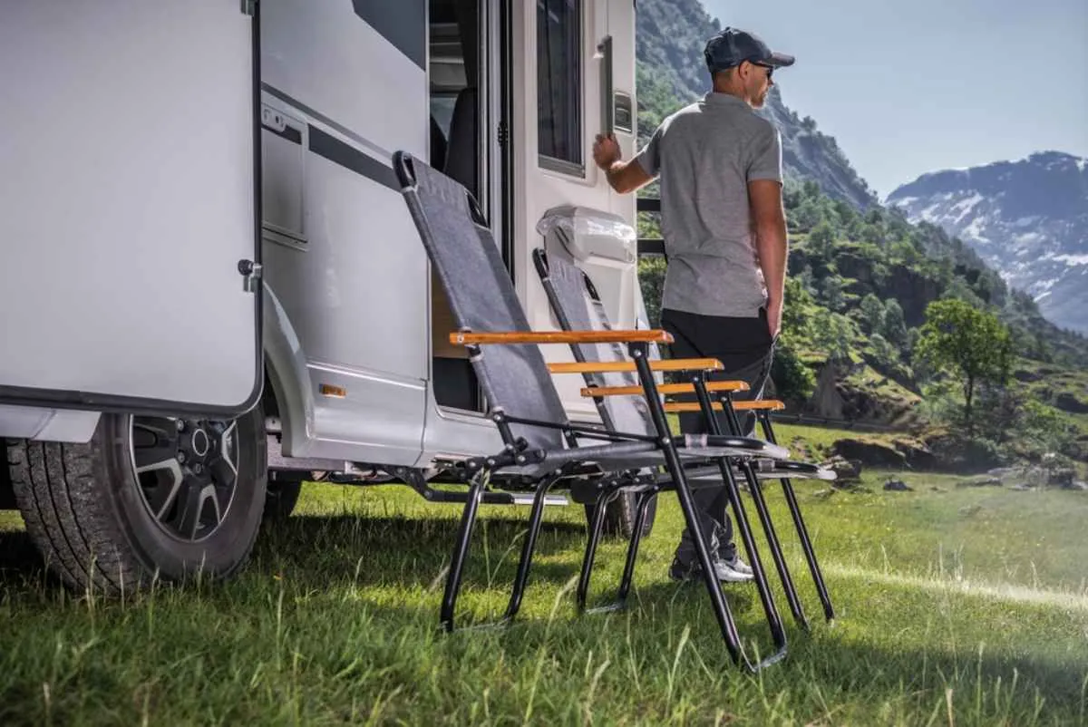 A man wearing a cap and short-sleeved T-shirt gets out of his camper parked in a Norwegian meadow on a sunny, cloudless day.