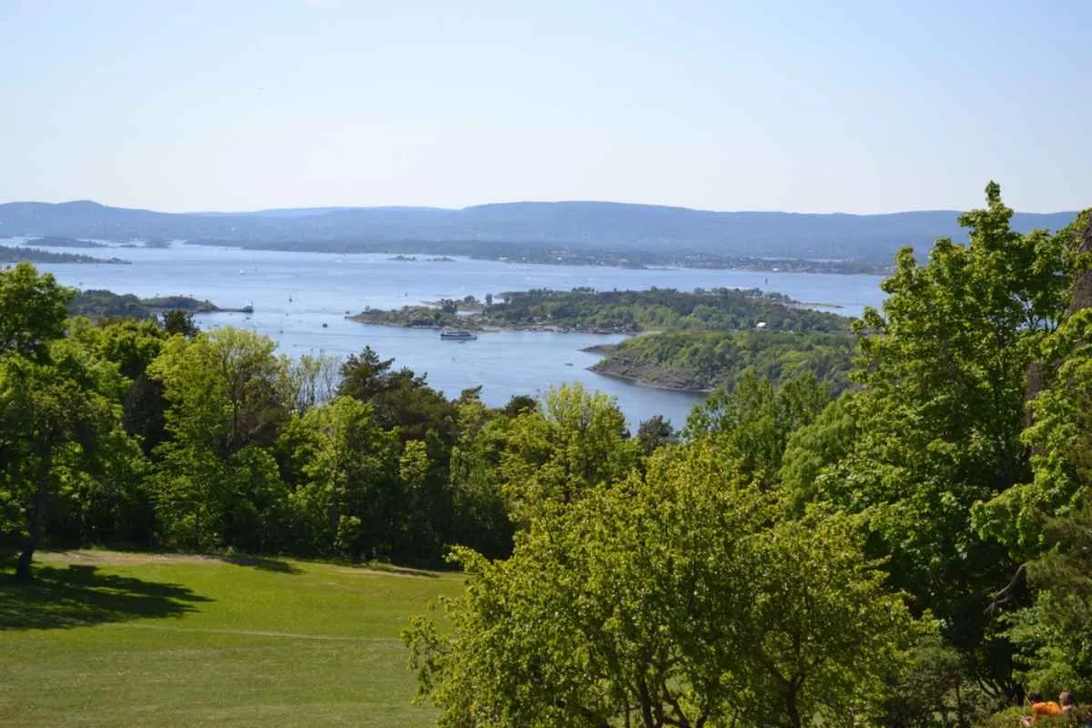 Aerial view of Ekerberg in Norway with green trees and crystal-clear water in the background that blends with the sky.