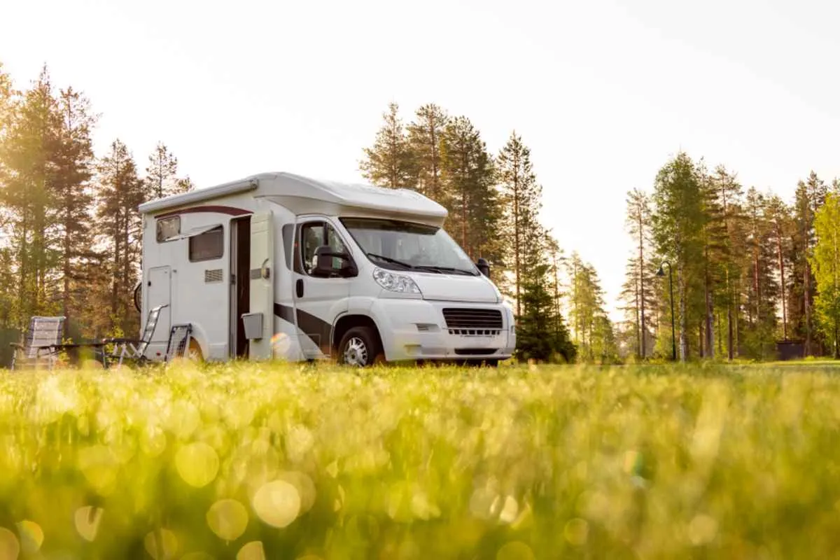 A white camper with chairs outside remains parked in a blurred green meadow.