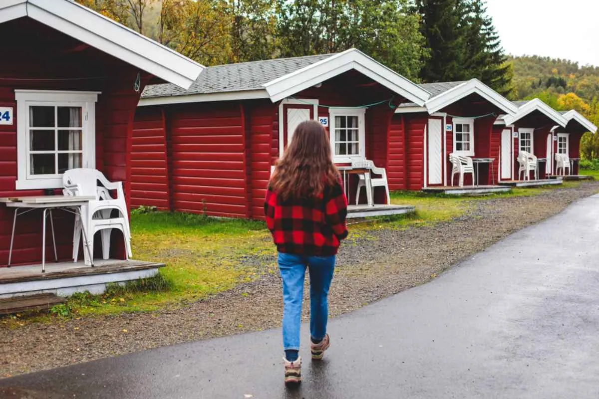 A person with long dark hair and a plaid shirt walks towards some camping houses in Norway of the same color.