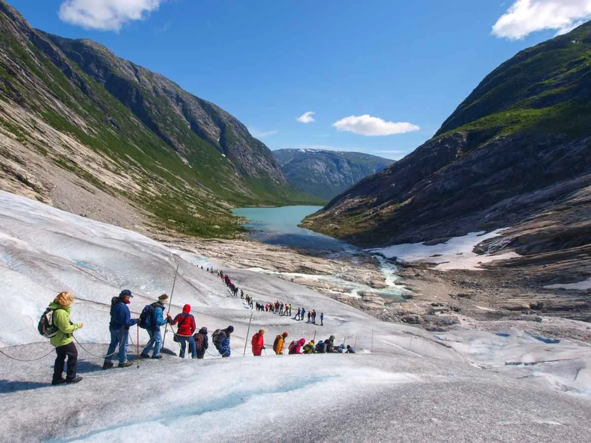 Dozens of hikers hike the glaciers of Norway's Jostedalsbreen National Park with the help of a rope and poles, and under practically cloudless skies.