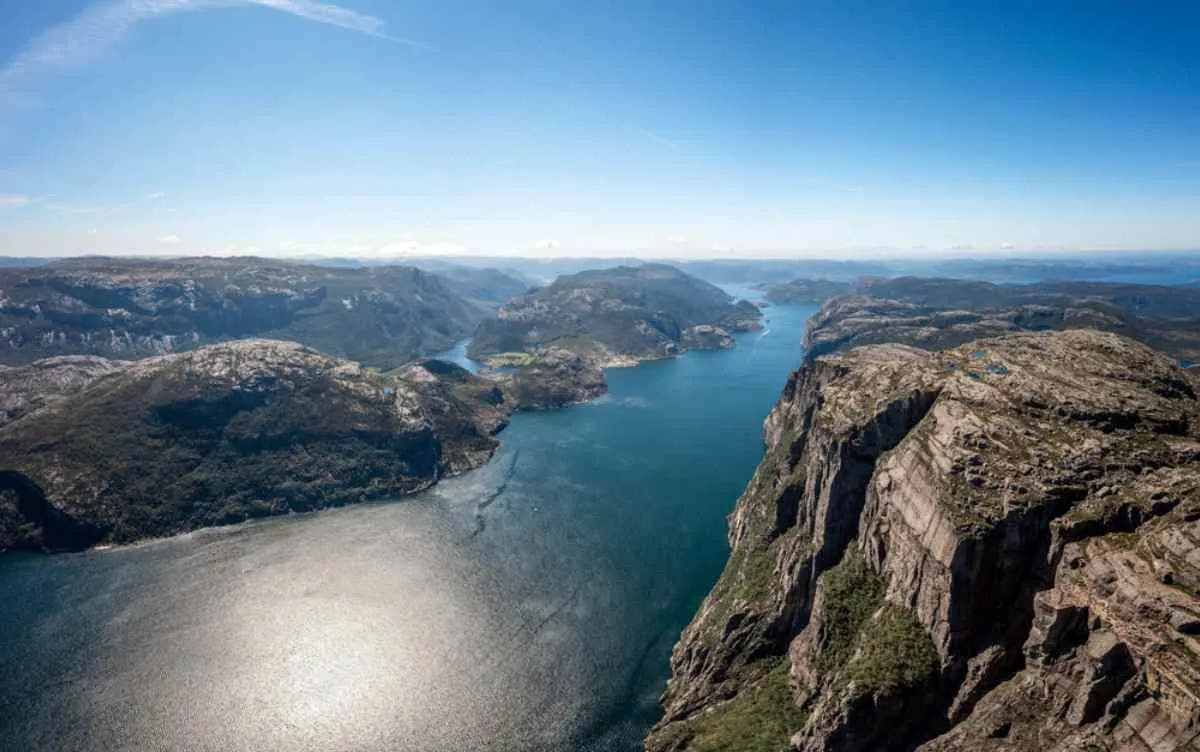 Aerial view of the Ryfylke archipelago under a clear sky and the sun reflected on the waters and the valley stretching between the high mountains.