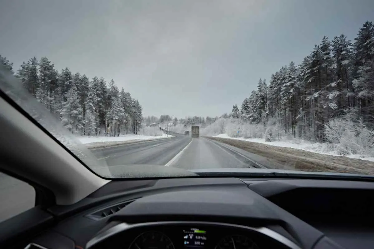 Interior of a car from the driver's perspective showing the vehicle's glass and the icy road with snow-covered trees.