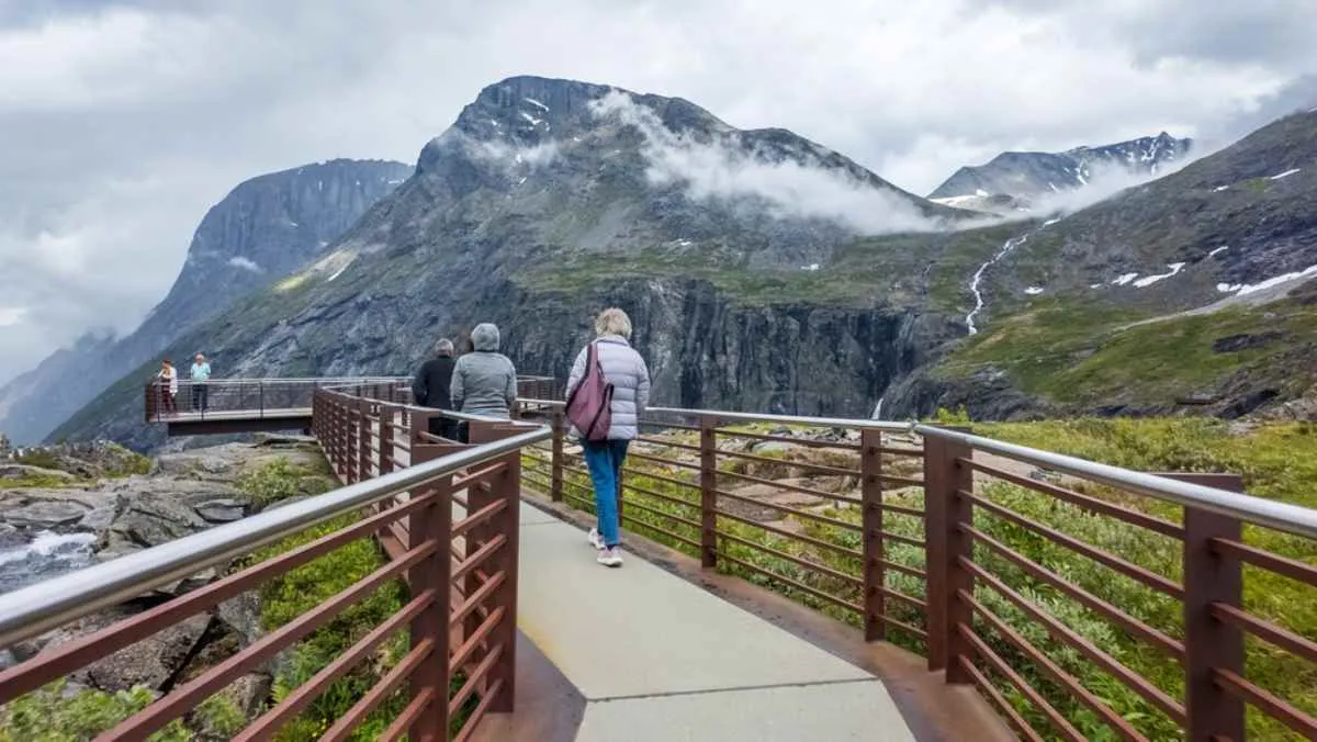 A group of people walk along the Visitor Center of Norway's Troll Road with cloud-covered mountains all around them.