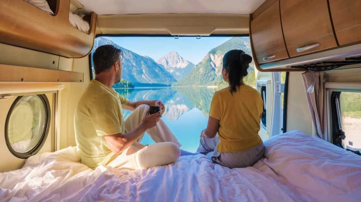 A couple on their backs enjoying a beautiful calm Norwegian lake from the comfort of the back of their camper.