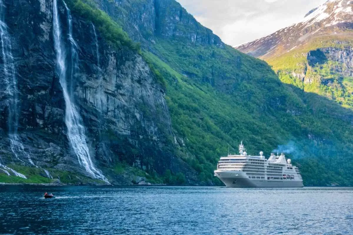 A huge cruise ship sails in front of a waterfall in Norway's Geirangerfjord.