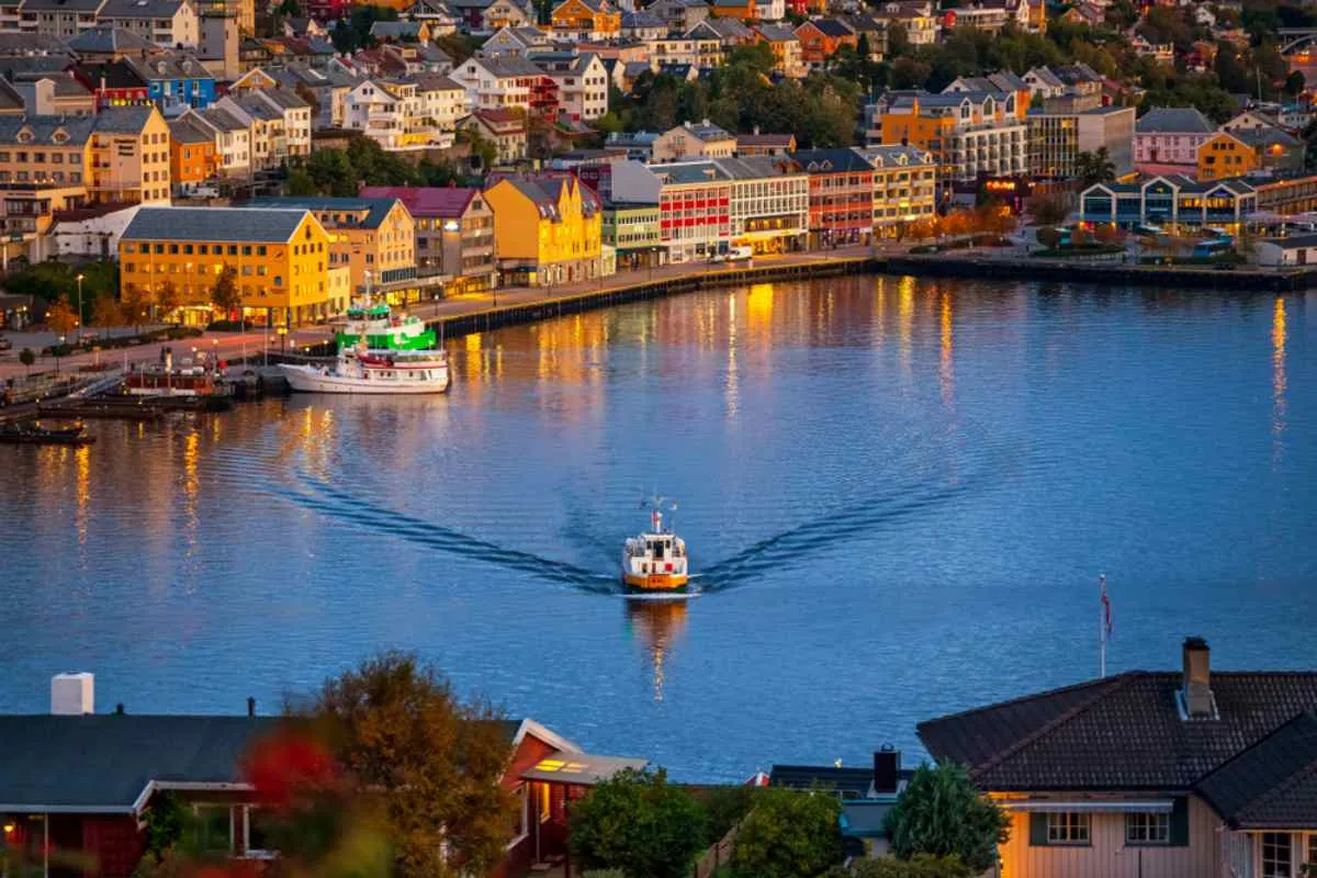Drom view of the city of Kristiansund in Norway with a boat sailing in the solitude of the city's bay as night approaches and the city's illumination is turned on.
