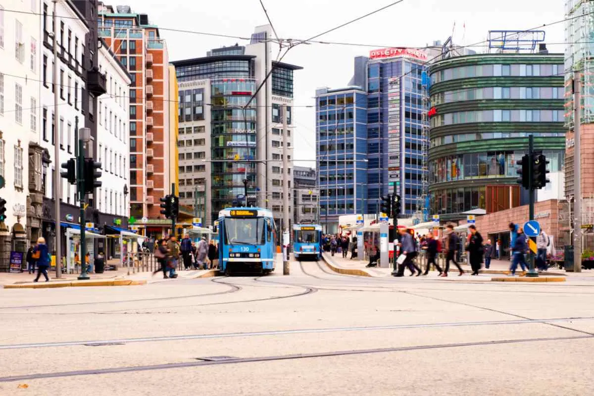 General view of a busy Oslo street in Norway with people crossing crosswalks and a couple of parked streetcars.