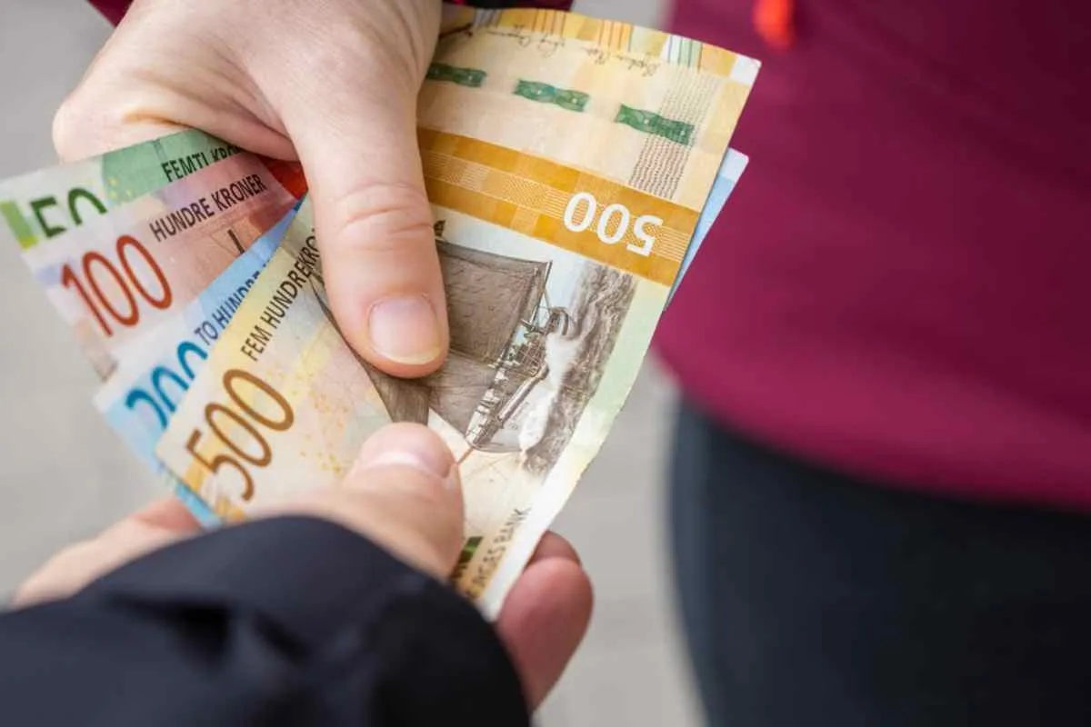 Close-up of the hands of two people handing each other a wad of Norwegian kroner banknotes.