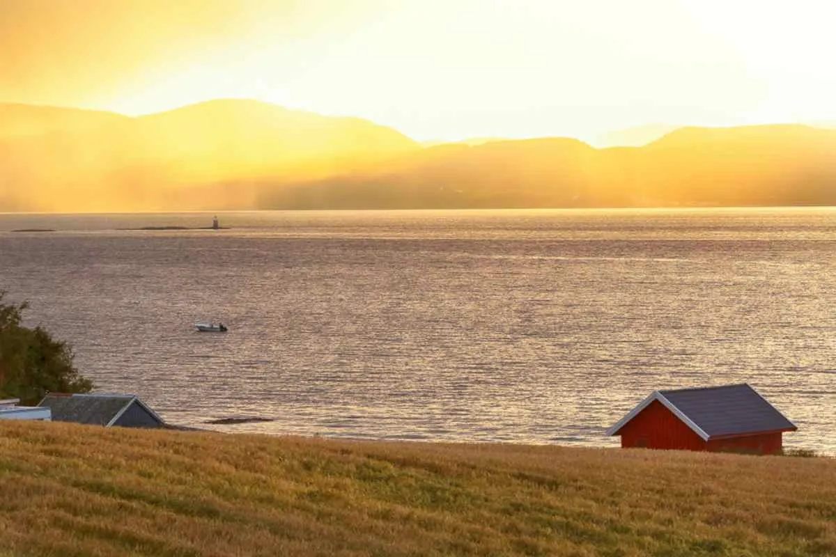 General view of a typical Norwegian redwood house near a fjord at sunset.