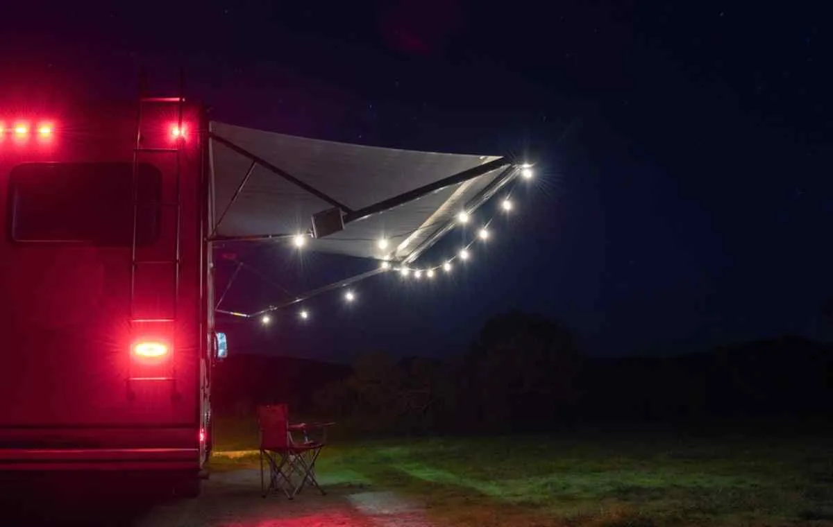 Overview of a motorhome parked in the middle of the night with the exterior lights on and a chair folded out on the makeshift porch.