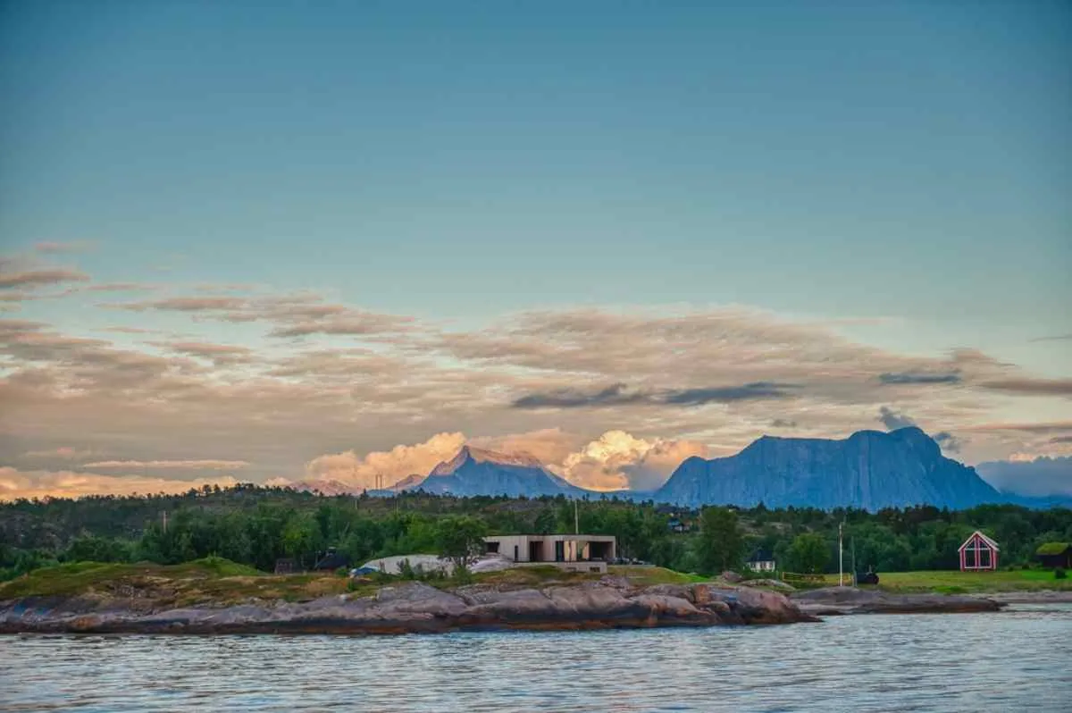 Overview of a beautiful lake near some cabins at the foot of the mountains in the distance during a sunset in Norway.