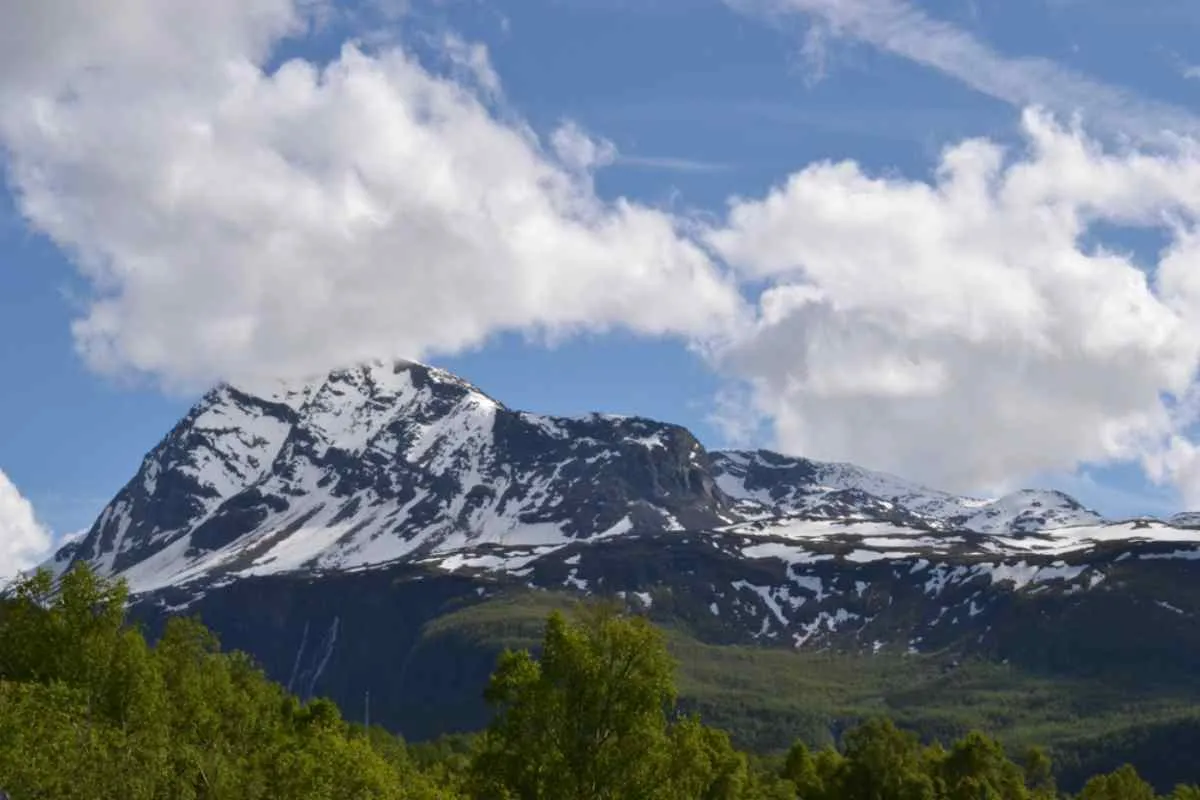 Close-up of the ridge of the Spanstind mountain in Norway completely covered by snow and partially by clouds.