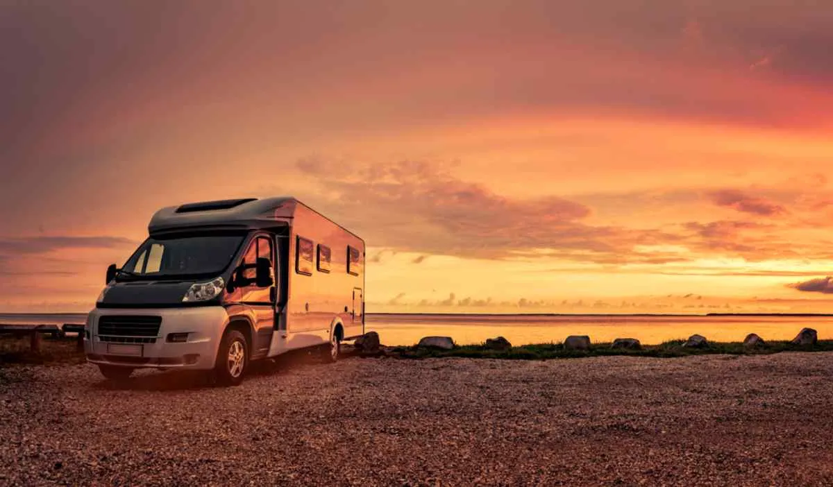 A motorhome appears parked at dusk in a quiet spot near a body of water.