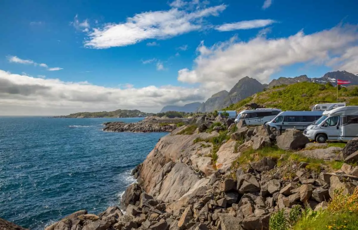 A pair of campers remain parked on a kind of cliff while the sea crashes against the rocks in front of them.