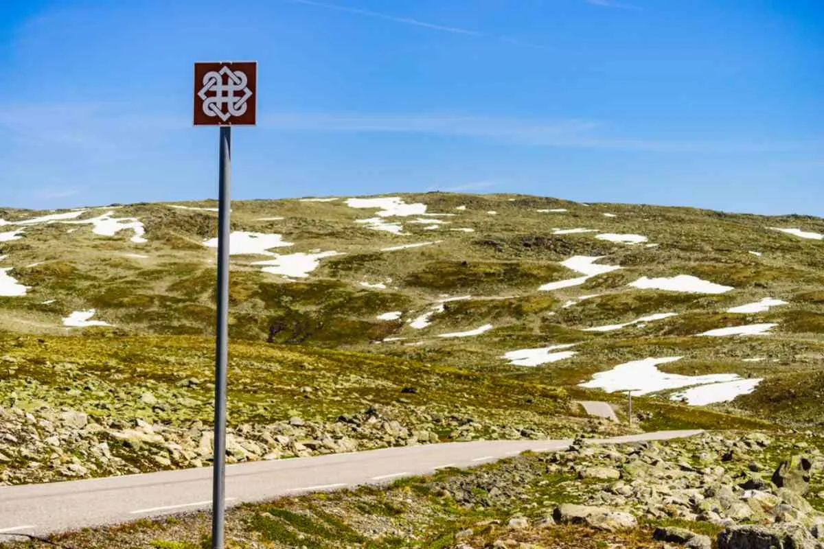 General view of a paved Norwegian road near a desert landscape with a sign erected with its distinctive icon indicating the proximity of an area of interest to tourists.