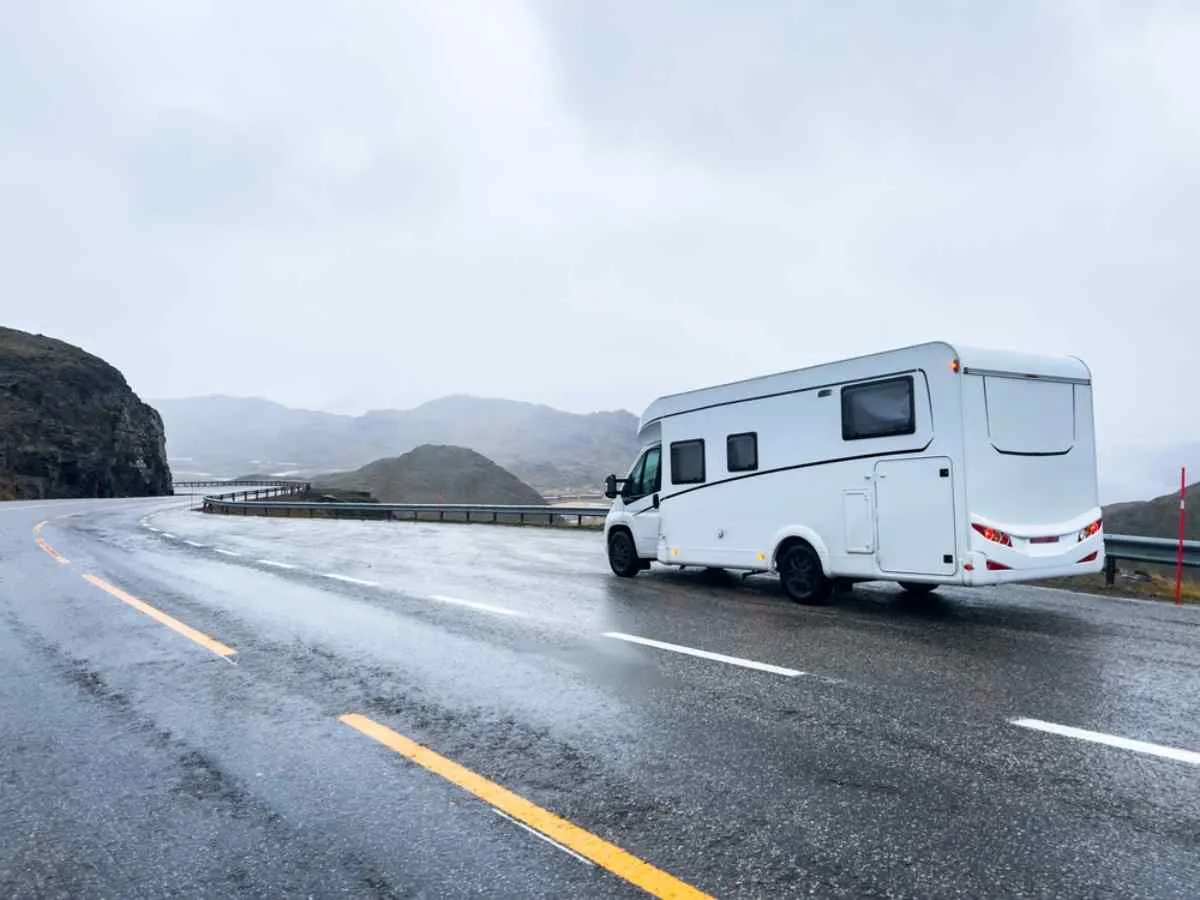 A white motorhome drives freely on a paved road in northern Norway.