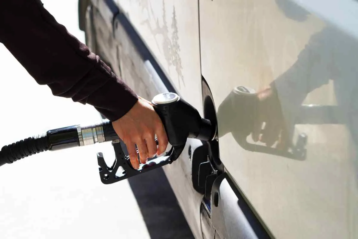 One hand holds a gas pump while it remains inside the tank of the parked campervan.