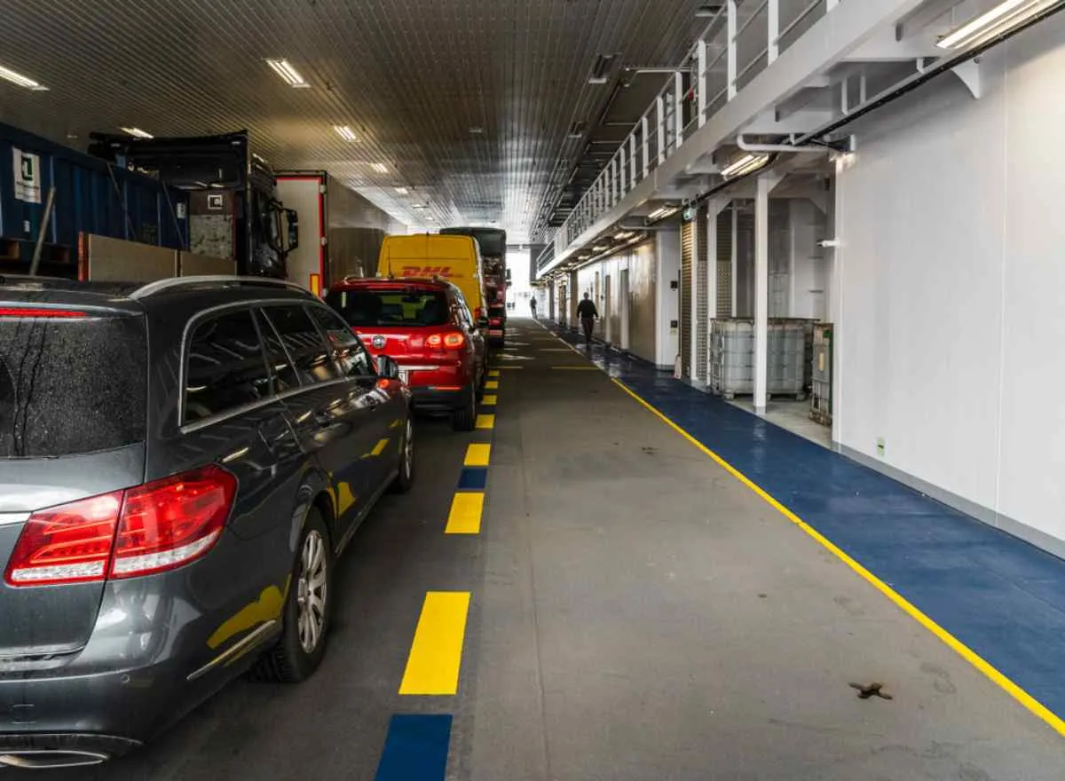 View of the interior of a ferry with a long line of vehicles riding on it waiting to reach their destination.