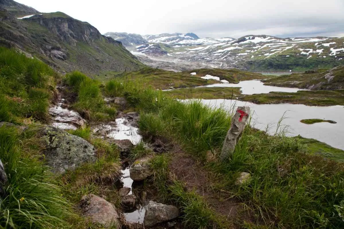 General view of a hiking trail located in the Hardangervidda area, Norway with bodies of water surrounding it and mountains in the distance.