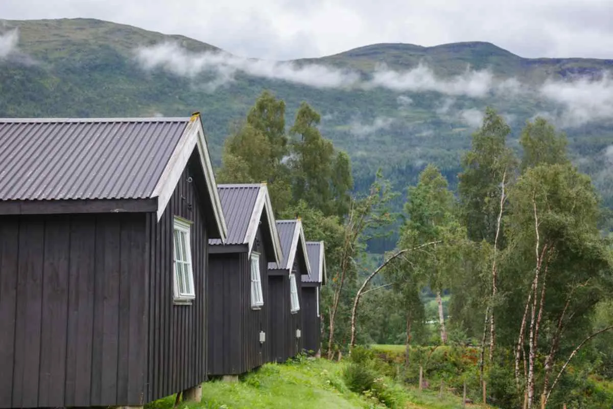 General view of a part of the typical Norwegian log cabins in what looks like a hilly and greenish landscape.