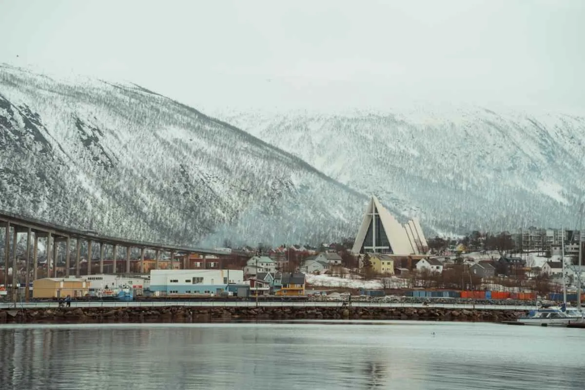 View of Tromsø’s waterfront with the Arctic Cathedral and bridge, snow-capped mountains behind.