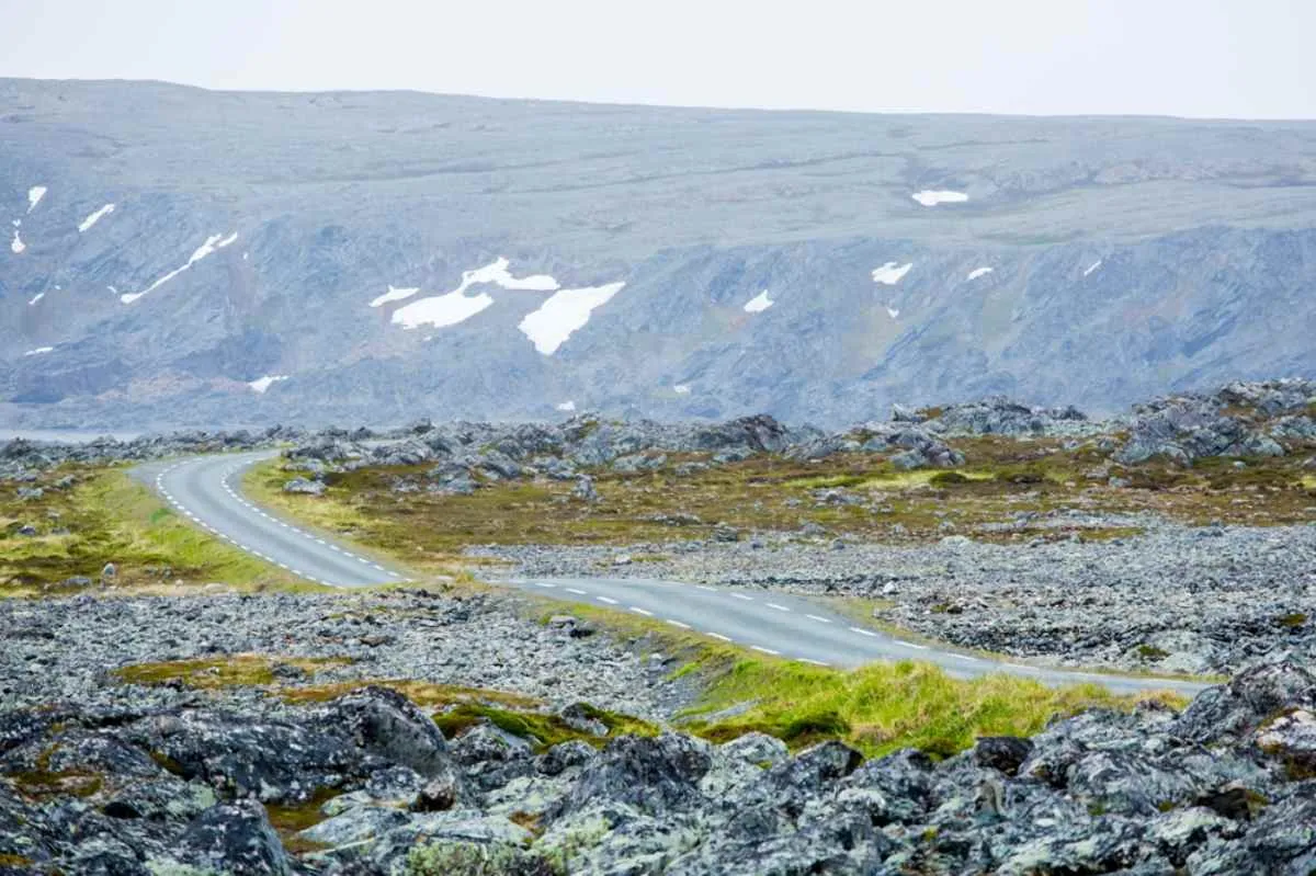 Rocky coastal landscape with sparse vegetation and a narrow road winding along the shoreline.