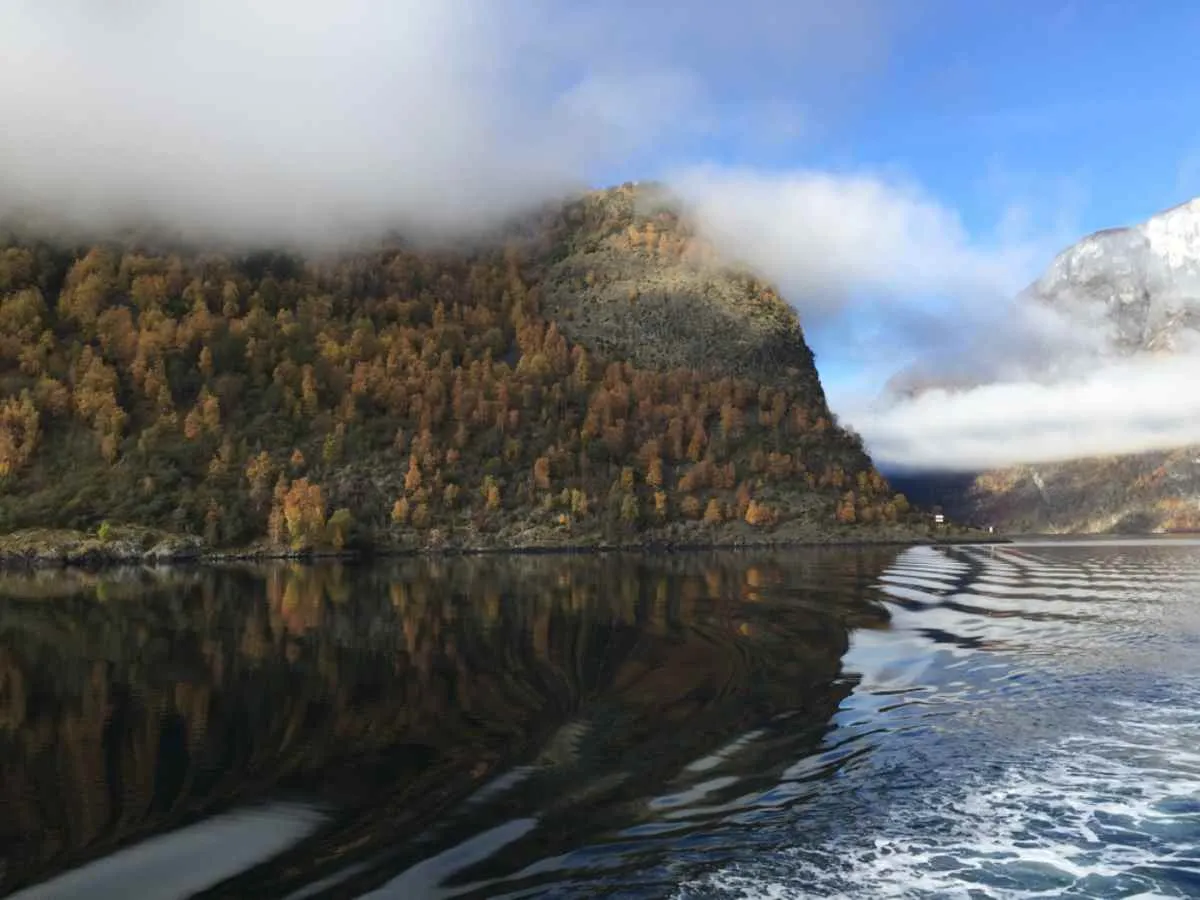 A view at water level of the Aurlandfjord in Norway, with somewhat turbulent waters and clouds covering the surrounding mountains.