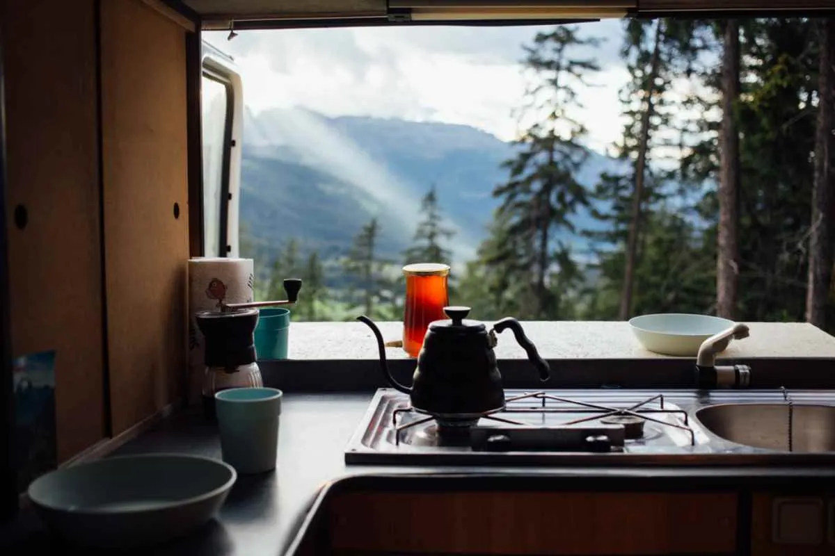 Simple campervan kitchen with kettle and cups looking out to forested mountains and valley.