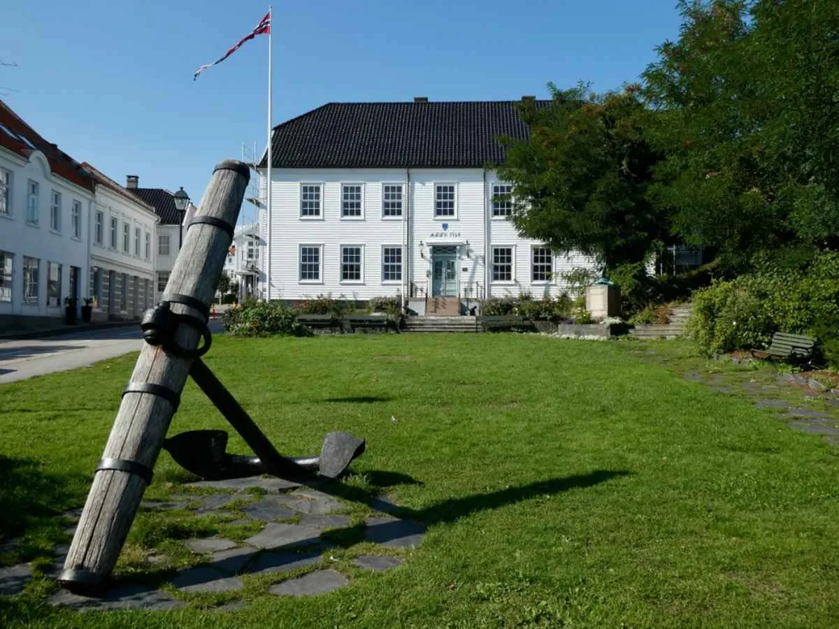 Historic white wooden house with a large anchor monument in Lillesand, Norway