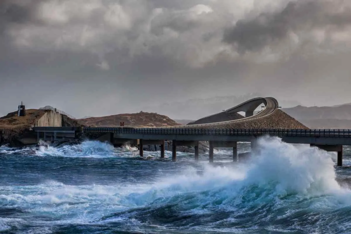Storm waves crash beneath the Storseisundet Bridge on Norway’s Atlantic Ocean Road, dramatic surf and brooding sky over the curving causeway.