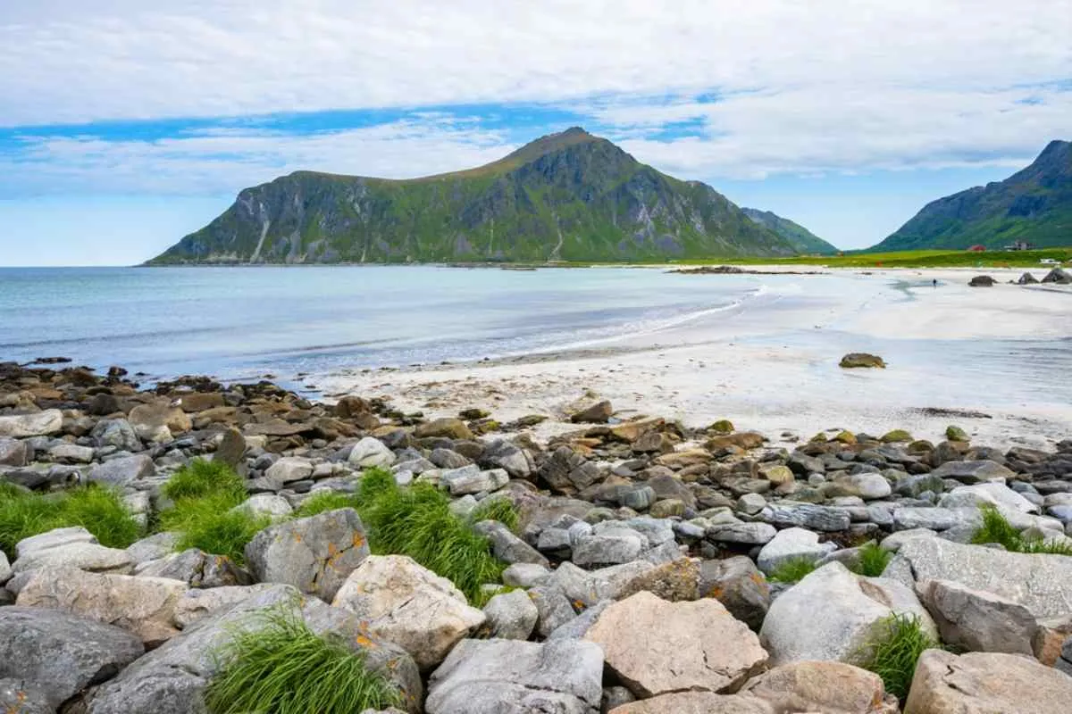 Rocky shoreline and white sandy beach at Skagsanden, framed by green mountains and calm Arctic waters in Lofoten.