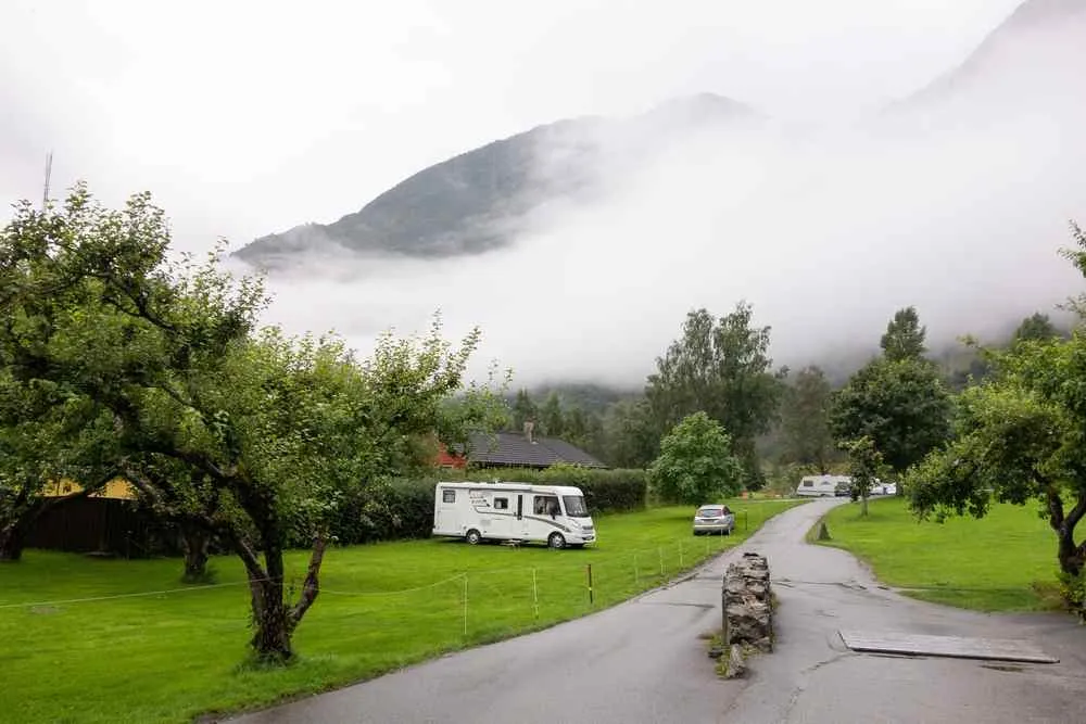 Motorhome on a grassy campground in Flåm with low clouds covering the surrounding mountains.