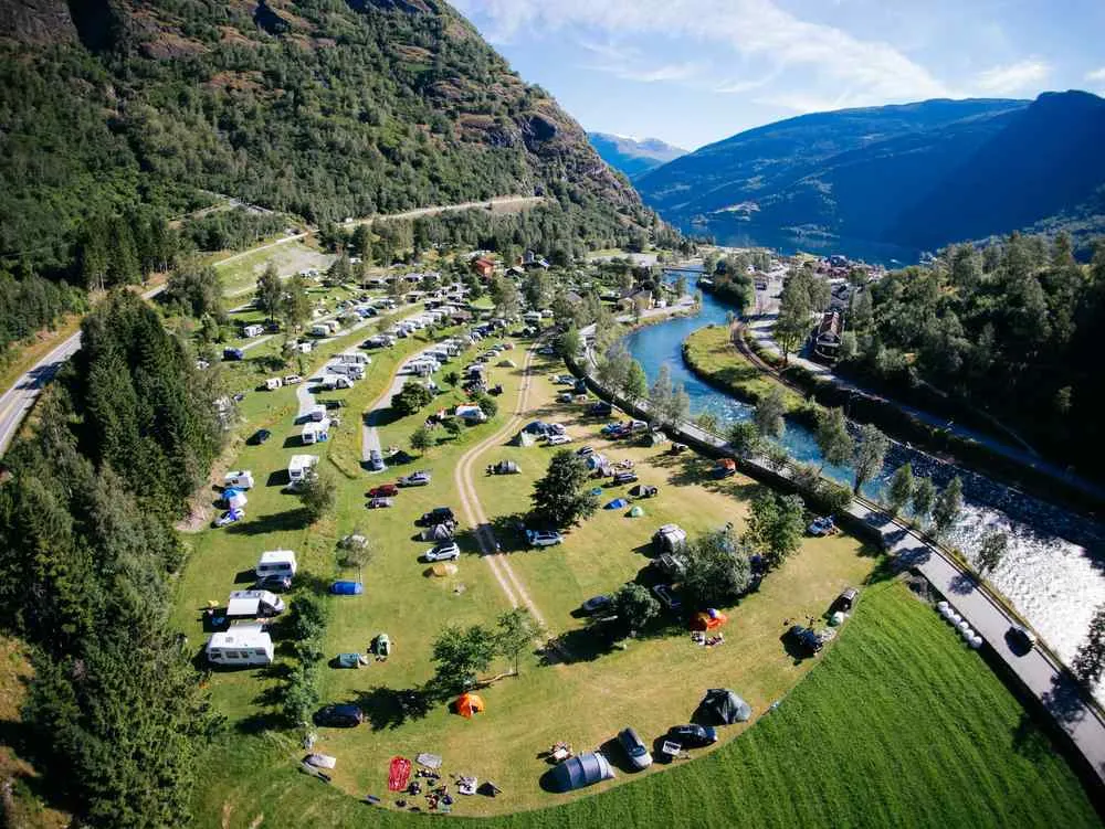 Aerial view of a riverside campsite in Flåm with tents, caravans, and motorhomes among the mountains.