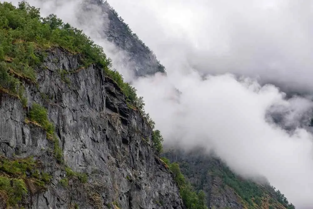 Low clouds drifting across rocky cliffs and forested mountains near Flåm, Norway.